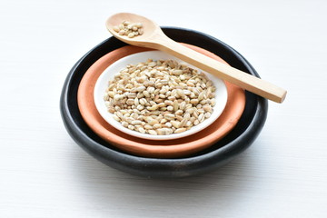 Raw barley grains, released in containers on white wooden background