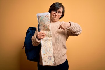 Young down syndrome tourist woman wearing bag and looking at destination city map with surprise...