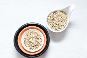 Raw barley grains, released in containers on white wooden background
