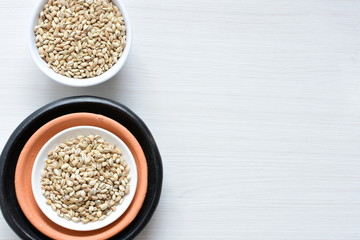 Raw barley grains, released in containers on white wooden background
