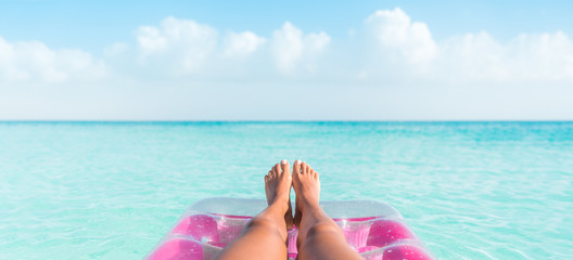 Beach summer vacation woman relaxing on pool float taking feet selfie pov of legs sunbathing relax on pink air mattress inflatable toy floating on blue ocean background panoramic banner. - obrazy, fototapety, plakaty