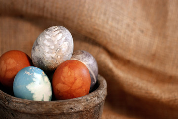 A collection of natural-dyed eggs with botanical leaf prints in a rustic gray clay pot against a...