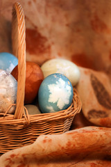 A wicker basket holding a collection of natural-dyed eggs with botanical leaf prints against a background of eco-printed silk, with copy space