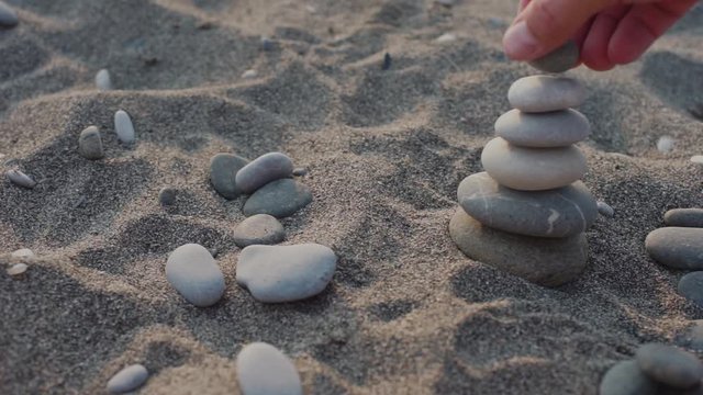 man builds on a sandy beach pyramids of pebbles, small stones. Balance and concentration. Hobbies. Relax on the beach. Business concept. Aspiration and calm. Soft focus and shallow depth of field.