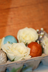 Obraz na płótnie Canvas Fresh white hybrid tea rose flowers and baby's breath (Gypsophila) with natural-dyed eggs with botanical leaf prints displayed in an egg carton against a burlap background, with copy space