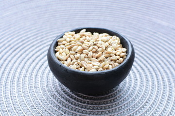 Raw barley grains, displayed in containers on textured background