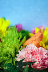 Closeup of a pink carnation, green spider mum, and other colorful florist flowers against a light blue background, with copy space