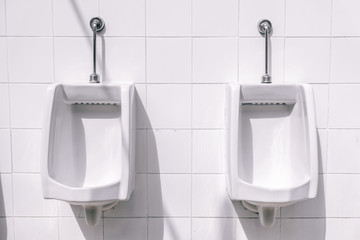 Two urinals on a white tiled wall in public restroom