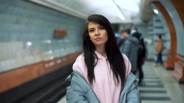 Young girl stands waiting for train at subway station, shows a fuck and laughs