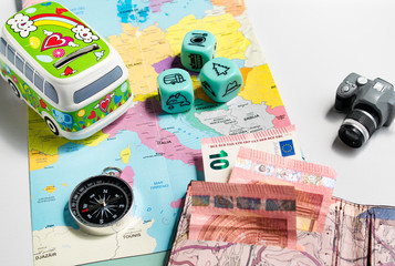map of europe, caravan shaped piggy bank, compass, money, toy photo camera and activity dice - concept of saving and planning for travel