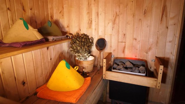Finnish Sauna traditional. Interior wooden empty Spa room Relaxation. Bath accesories stones, massage, towels, hat, bucket, broom, ladle.