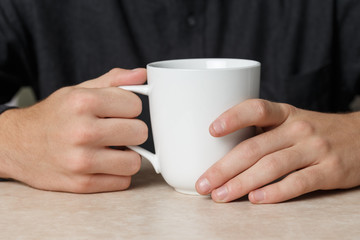 Young Caucasian Man Casually Holding White Cup of Tea or Coffee On Counter Or Table in Diner