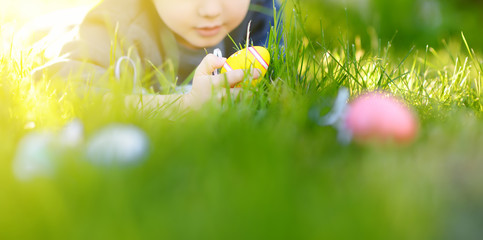 Little boy hunting for easter egg in spring garden on Easter day. Focus on multicolor eggs.