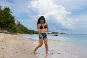 use of medical face mask in public places- young attractive Asian Chinese woman enjoying beach holidays in bikini and protective facial mask in prevention vs virus infection