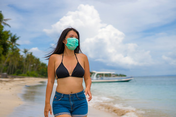 use of medical face mask in public places- young attractive Asian Chinese woman enjoying beach...
