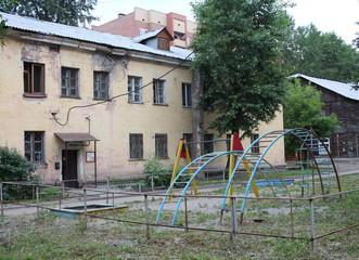 Obraz na płótnie Canvas an old apartment building with a ruined facade dirty children's Playground with a swing set in the yard in the fall