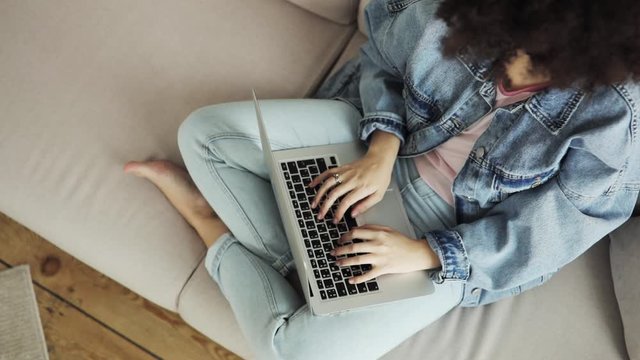 Woman is working writing typing on laptop sitting on sofa, top view. She is working on computer at home. Freelancer is making her job. Chatting in messenger with friends in social media.