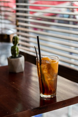 peach iced tea in a glass with slices of peach, wooden table and window blinds in the background