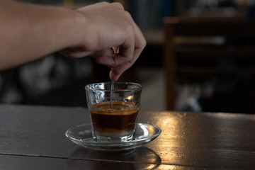 man's hand stirring vietnamese style coffee with glass saucer on wooden table in a coffee shop