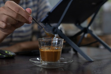 man's hand stirring vietnamese style coffee with glass saucer on wooden table in a coffee shop