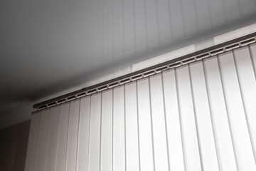 Part of the mechanism of beige vertical blinds on the background of a mirror stretch ceiling.