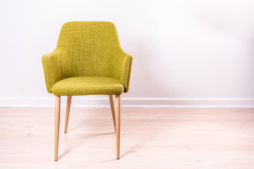 Close up of a stylish green chair with light wooden legs, in front of a white wall, on very light hard wood floors.