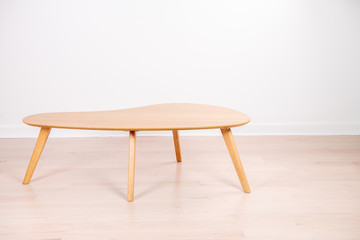 Close up of a cute, retro style coffee table, made of light oak wood, in front of a white wall.