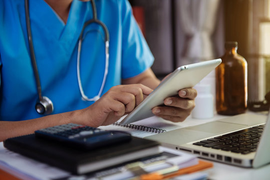 Male Doctor Working On Desk With Laptop Computer And Paperwork In The Office. Medical And Doctor Concept.