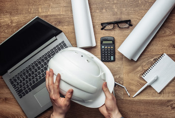 Engineer workspace. Men's hands holding construction helmet on the background of workplace. Top view