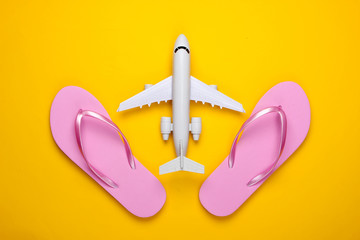 Travel flat lay composition. Plane figurine, flip flops on a yellow background. Beach vacation. Top...