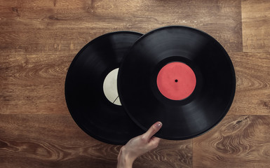 Obraz premium Female hand holds two vinyl records on a wooden floor. Top view