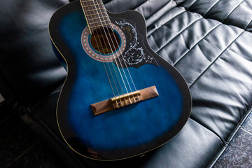 Fototapeta premium A wooden blue guitar lies on a black sofa