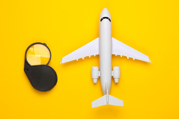 Flat lay travel composition. Airplane figurine and magnifier on a yellow background. Top view....