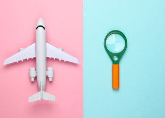 Flat lay design of travel concept with plane and magnifier. Pink blue pastel background. Minimalism. Top view