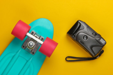 Summer fun. Youth flat lay. Cruiser board with a retro camera on a yellow background. Retro 80s. Top view