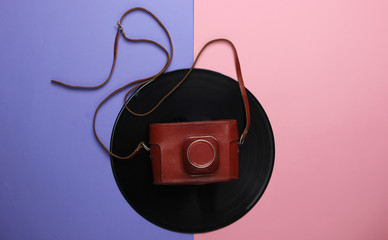Vinyl record with a retro camera on a purplish pink pastel background. Top view