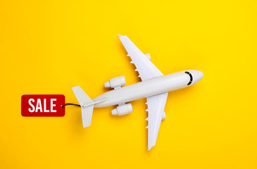 Airplane figurine with red sale tag on yellow background. Top view. Discount. Minimalism