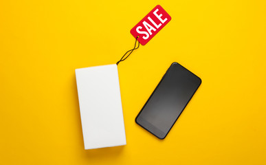 New smartphone and box with tag sale on a yellow background. Top view