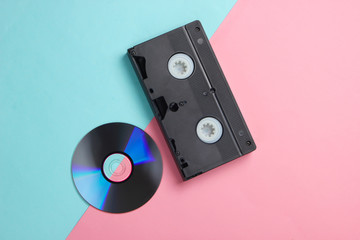 Flat lay composition of cd disc, audio cassette on pink blue background. Retro storage media. Top...