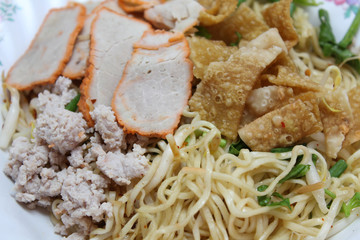 Close up view of dried egg noodles in a bowl mix topping with red pork, minced pork, onion and fried wonton sheet, Chinese cuisine