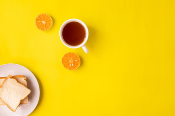 Obraz na płótnie Canvas Sliced orange fruit, cup of tea and bread on yellow background.