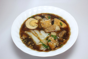 Chinese roll noodle soup (Guay Jub Nam Kon call in Thai) with crunchy pork, egg and cinnamon in white bowl on white background, it’s one of the top Thai street food dishes to try