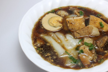 Chinese roll noodle soup (Guay Jub Nam Kon call in Thai) with crunchy pork, egg and cinnamon in white bowl on white background, it’s one of the top Thai street food dishes to try
