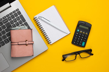 Economic calculation, profit analysis, family budget concept. Laptop, wallet, notebook, glasses, calculator on a yellow background. Workspace. Top view