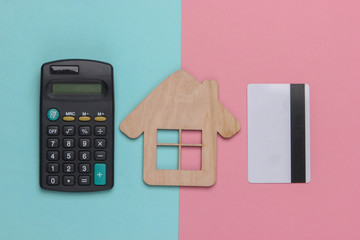 Calculation of rents or house purchases. Calculator and bank card, house figurine on a blue-pink...