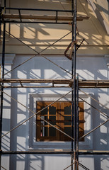 Sunlight and shadow on surface of the old scaffolding in front of wooden window on concrete wall of house building structure under renovate and construction in vertical frame, selective focus