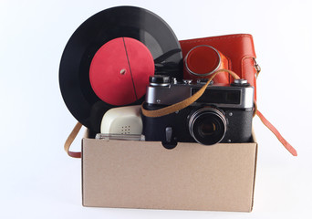 Cardboard box with retro film camera, gamepad,  vinyl record, phone tube on a white background....