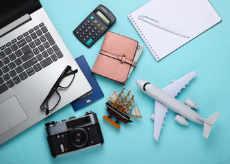 Travel concept. Calculation of the cost of vacation. Laptop, plane figurine, ship, calculator and traveler accessories on blue background. Top view. Flat lay
