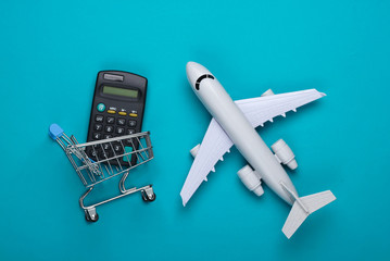 Flat lay composition. Cost calculation of Air delivery, shopping, logistics. Figurine of shopping trolley, airplane, calculator on blue background. Top view