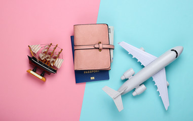 Flat lay travel design. Figurine of a ship, airplane, passport and walet on a blue-pink pastel background. Top view
